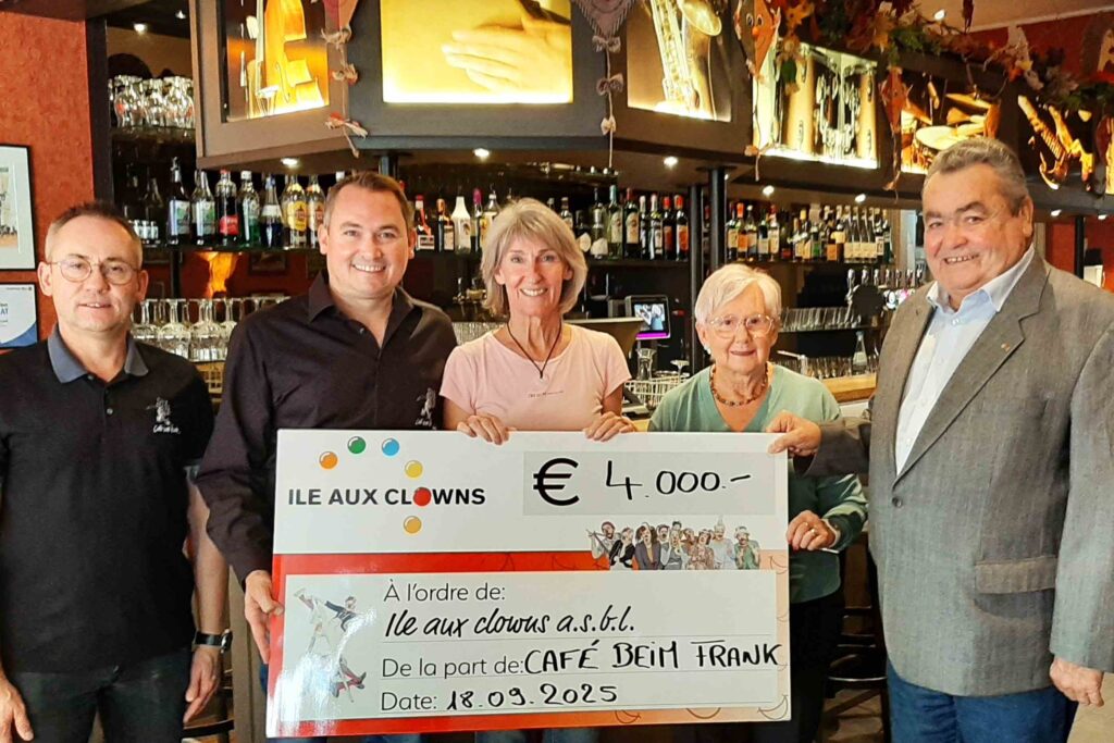 Cinq personnes se tiennent debout dans un bar, souriantes, tenant un gros chèque symbolique de 4 000 € à l'ordre de l'association « Ile aux clowns a.s.b.l. ». L'ambiance est chaleureuse, avec des bouteilles et des verres visibles en arrière-plan.