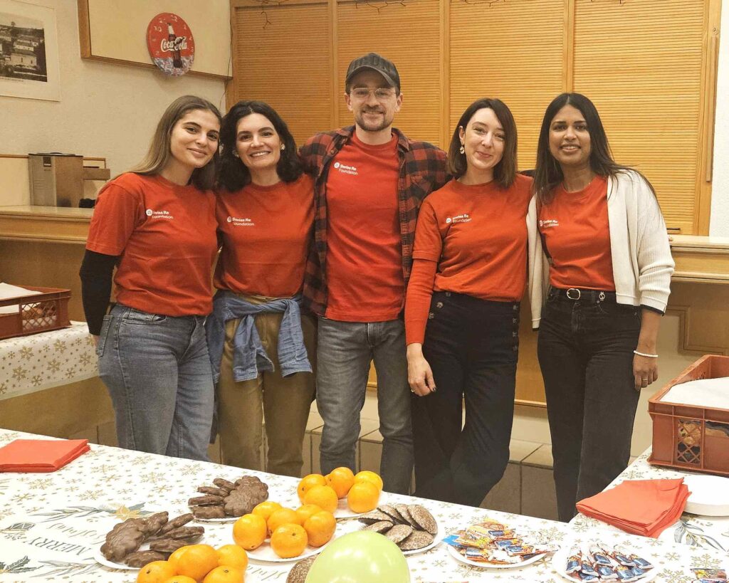 Cinq personnes vêtues de t-shirts rouges assortis se tiennent côte à côte et sourient dans une pièce où l'on aperçoit, au premier plan, une table garnie de fruits et de friandises.